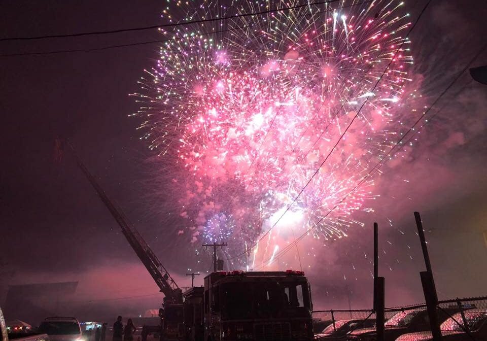 fireworks in the sky with fire truck silhouettes below