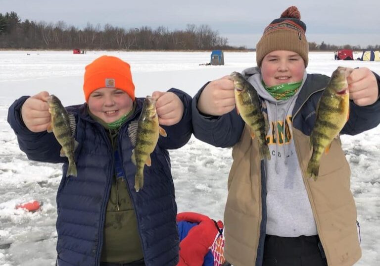 kids holding perch with ice fishing equipment in the background