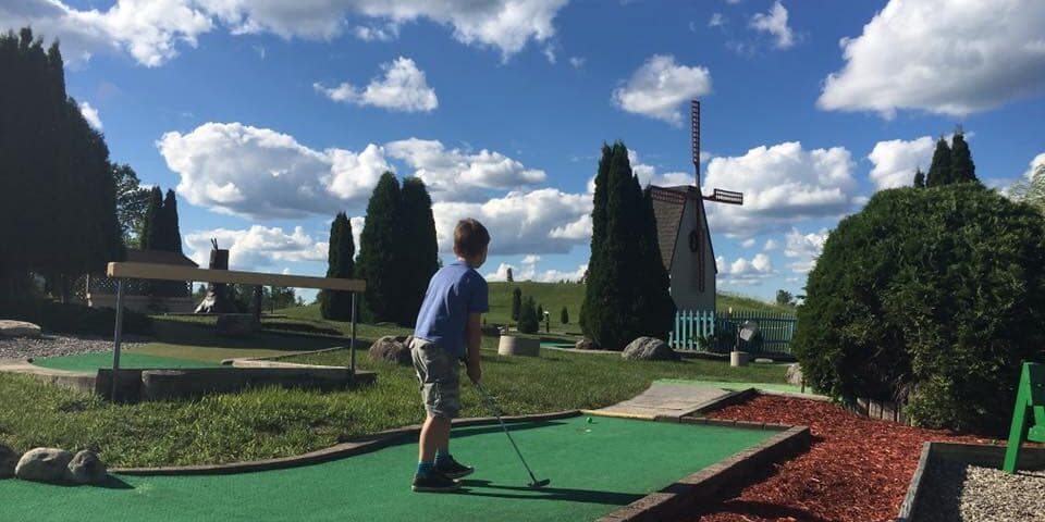 little kid playing putt putt golf on a sunny day