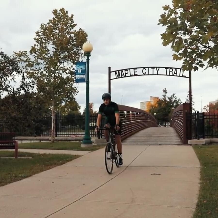 man riding a bike under the maple city trail sign in ogdensburg