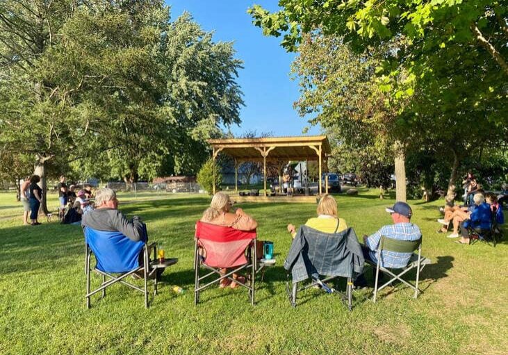 people sitting in chairs at the park watching live music