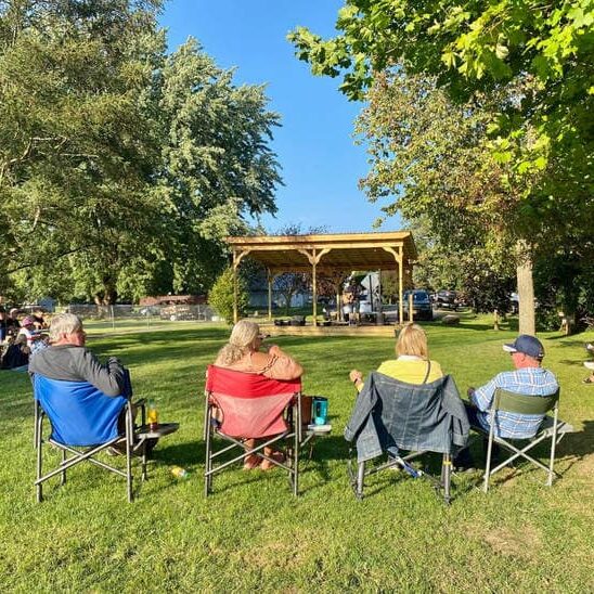 people sitting in chairs at the park watching live music
